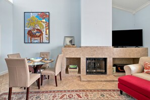 A living room with a fireplace, a television, a dining table with chairs, and a colorful painting on the wall.