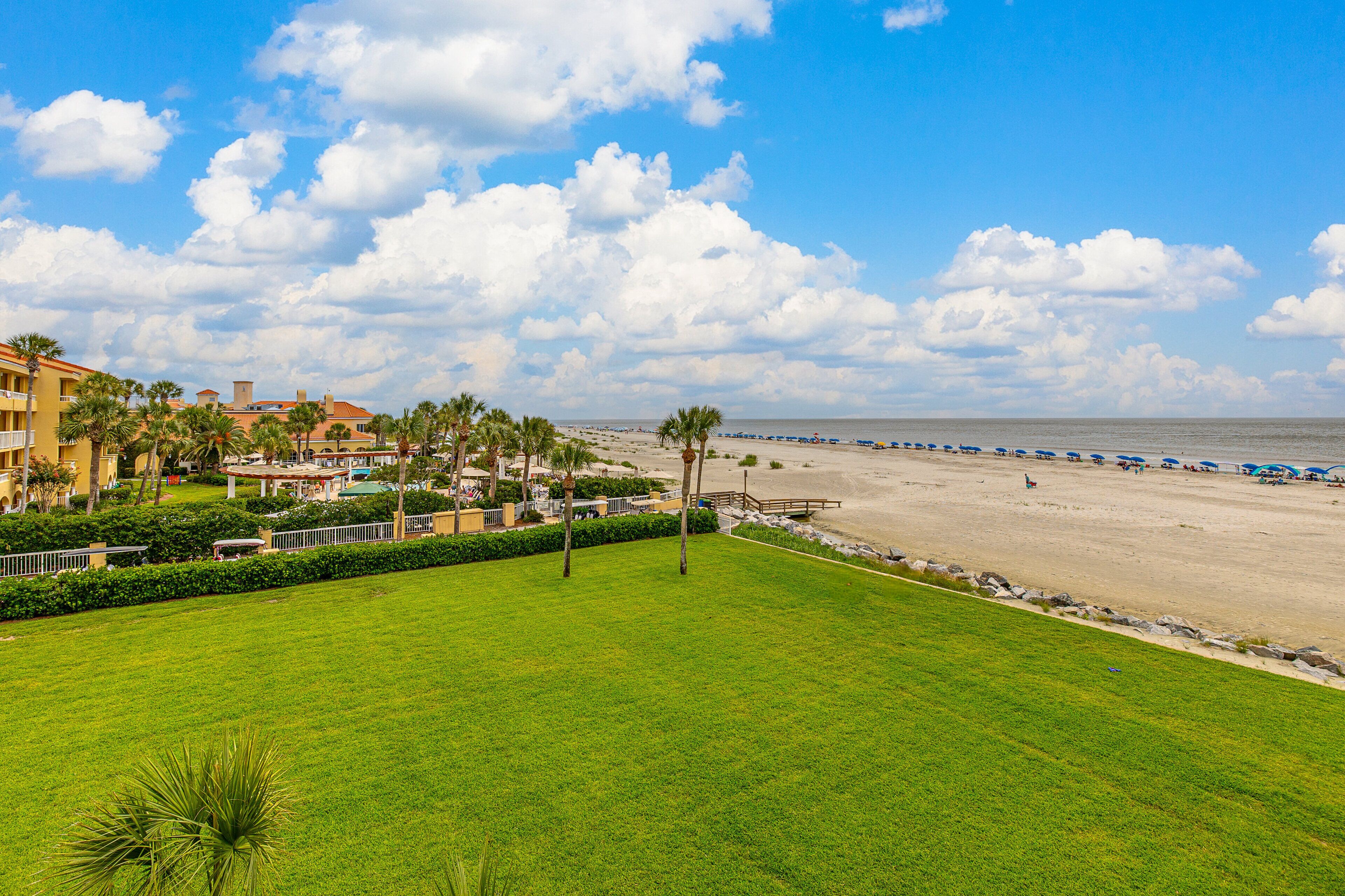 A beach resort with a grassy lawn, palm trees, and a view of the ocean.