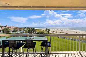 A balcony with a table and chairs overlooking a beach with a clear sky.