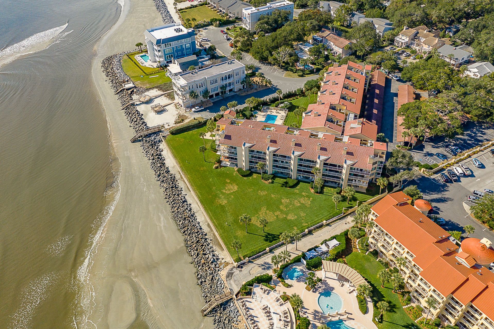 Vista aérea de um hotel à beira-mar, com vários edifícios, piscina e praia.