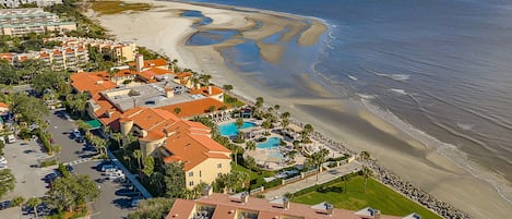 A coastal hotel with multiple buildings, a swimming pool, and a beach.