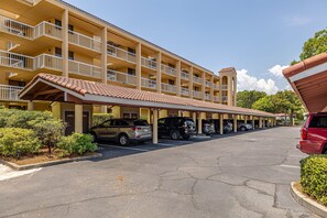 A multi-story hotel with balconies, a covered parking area, and a clear sky.