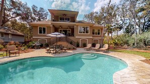 Ein zweigeschossiges Haus mit Swimmingpool, Sitzgelegenheit im Freien und einer überdachten Terrasse.