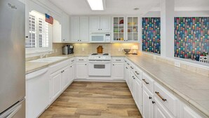 A kitchen with white cabinets, a stove, a microwave, and a window with blinds. - Feel the Coastal Breeze from your Porch! (Saint Simons Island)