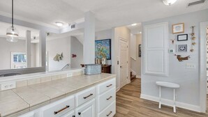 A modern kitchen with white cabinetry, a large island, and a wooden floor. - Feel the Coastal Breeze from your Porch! (Saint Simons Island)