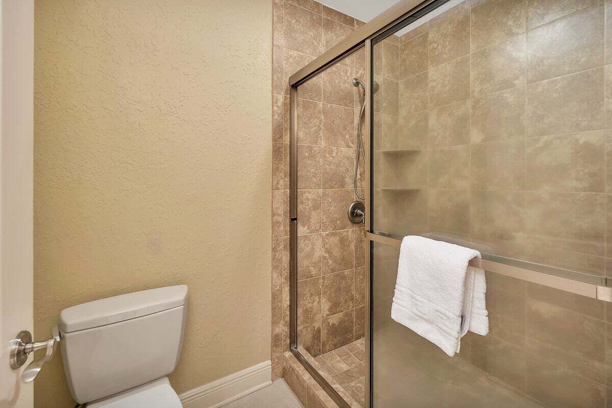 Un baño con cabina de ducha de vidrio, paredes color beige y una toalla blanca colgada en la pared.