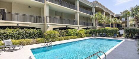A multi-story hotel with a swimming pool, outdoor seating, and palm trees.