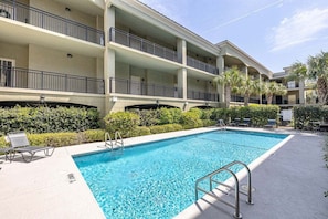 Hotel com piscina, várias varandas e palmeiras.