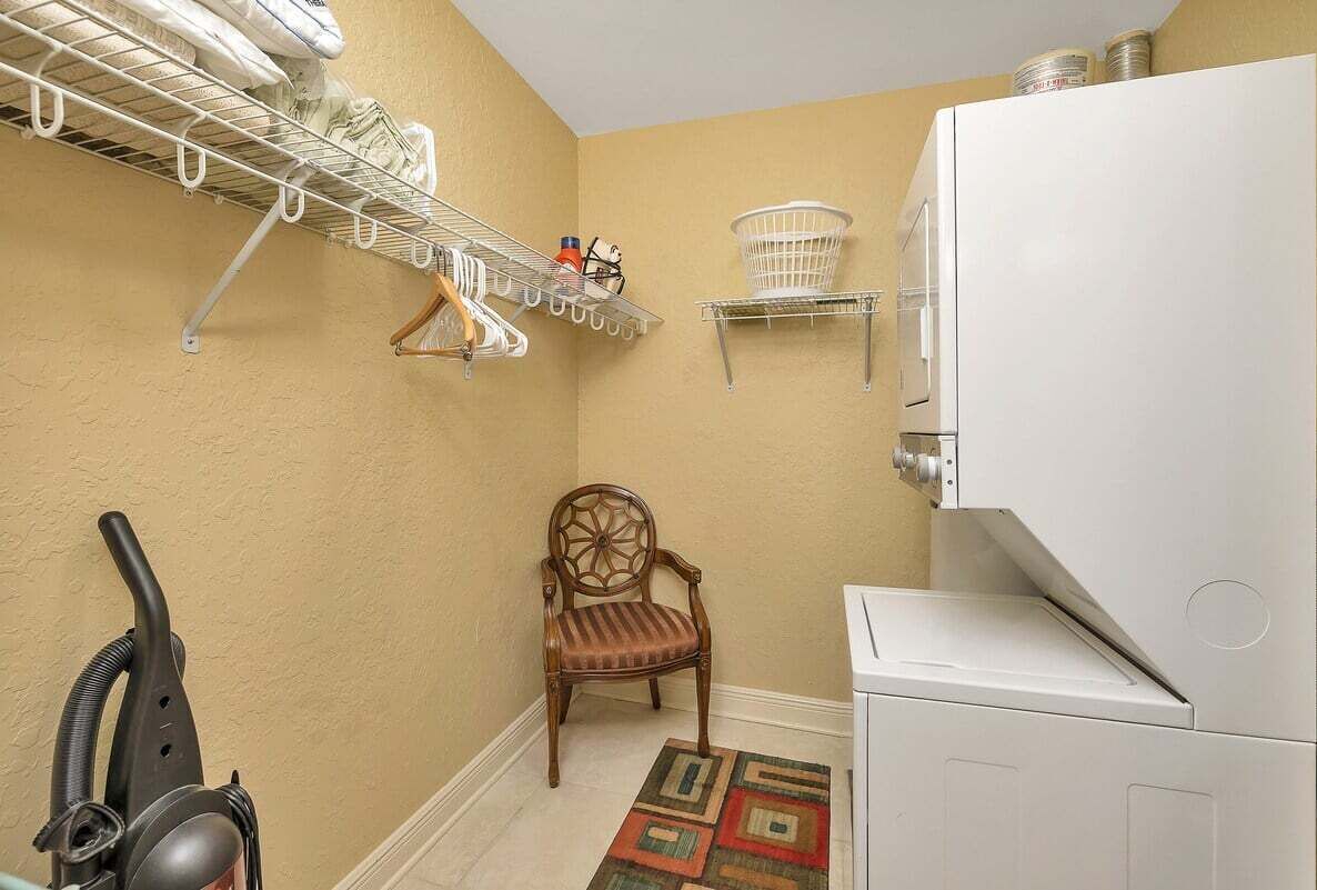 A laundry room with a washing machine, a drying rack, a chair, and a vacuum cleaner.