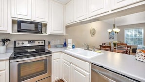 Una cocina con armarios blancos, microondas, estufa, horno, fregadero y una zona de comedor con sillas y mesa.