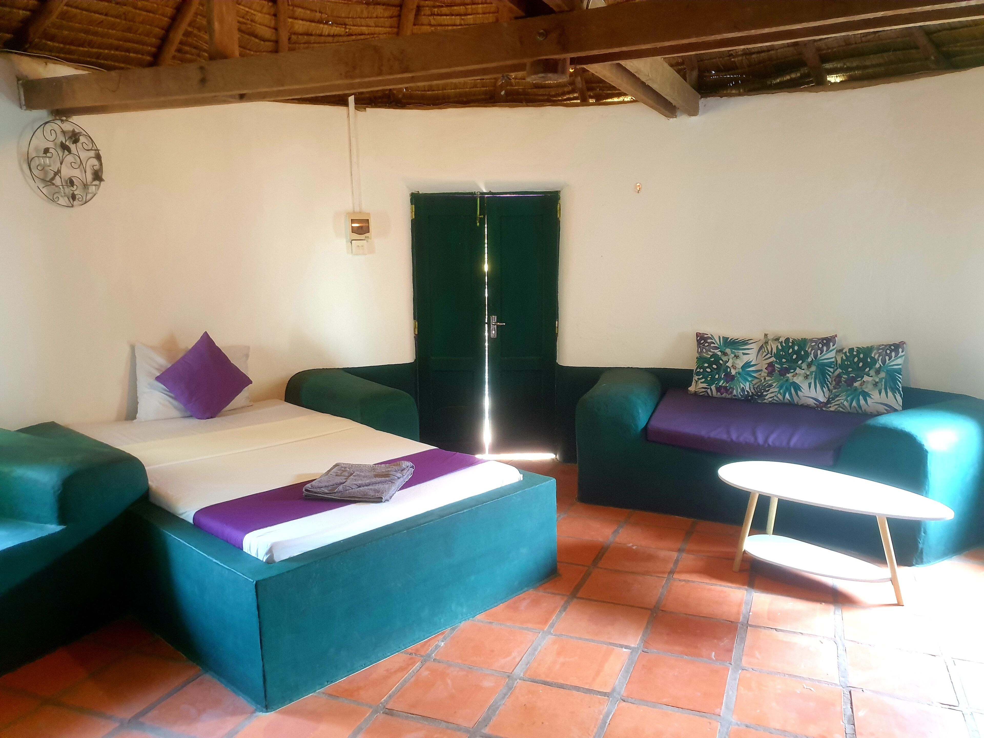 A room with a bed, two sofas, a small table, and a green door.