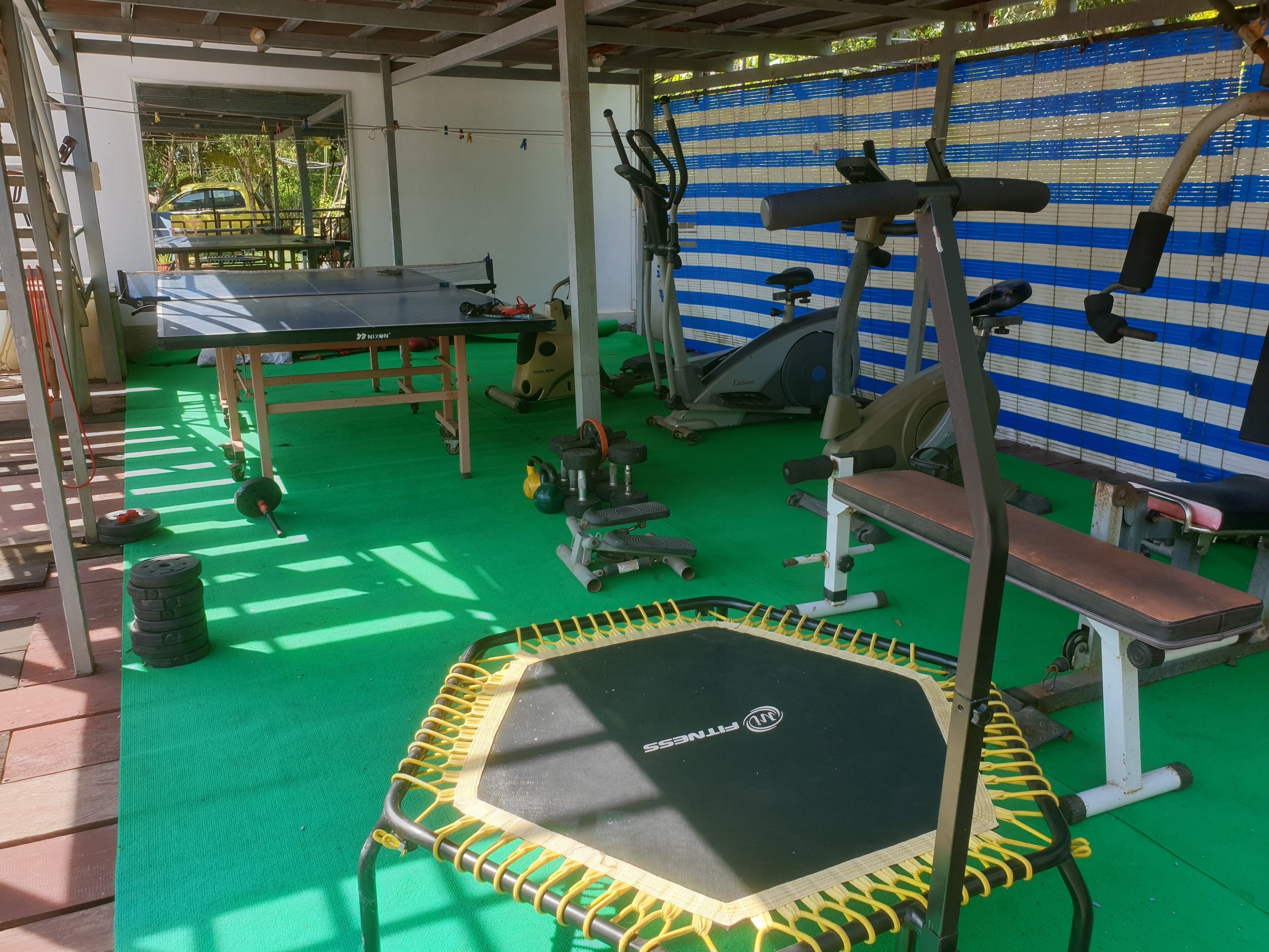 Un gimnasio con diferentes equipos de ejercicio, incluyendo un trampolín, máquinas de pesas y una banca.