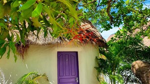 A small, single-story building with a purple door, surrounded by lush greenery and a thatched roof structure. - Bohemiaz Resort and Spa (Kampot)