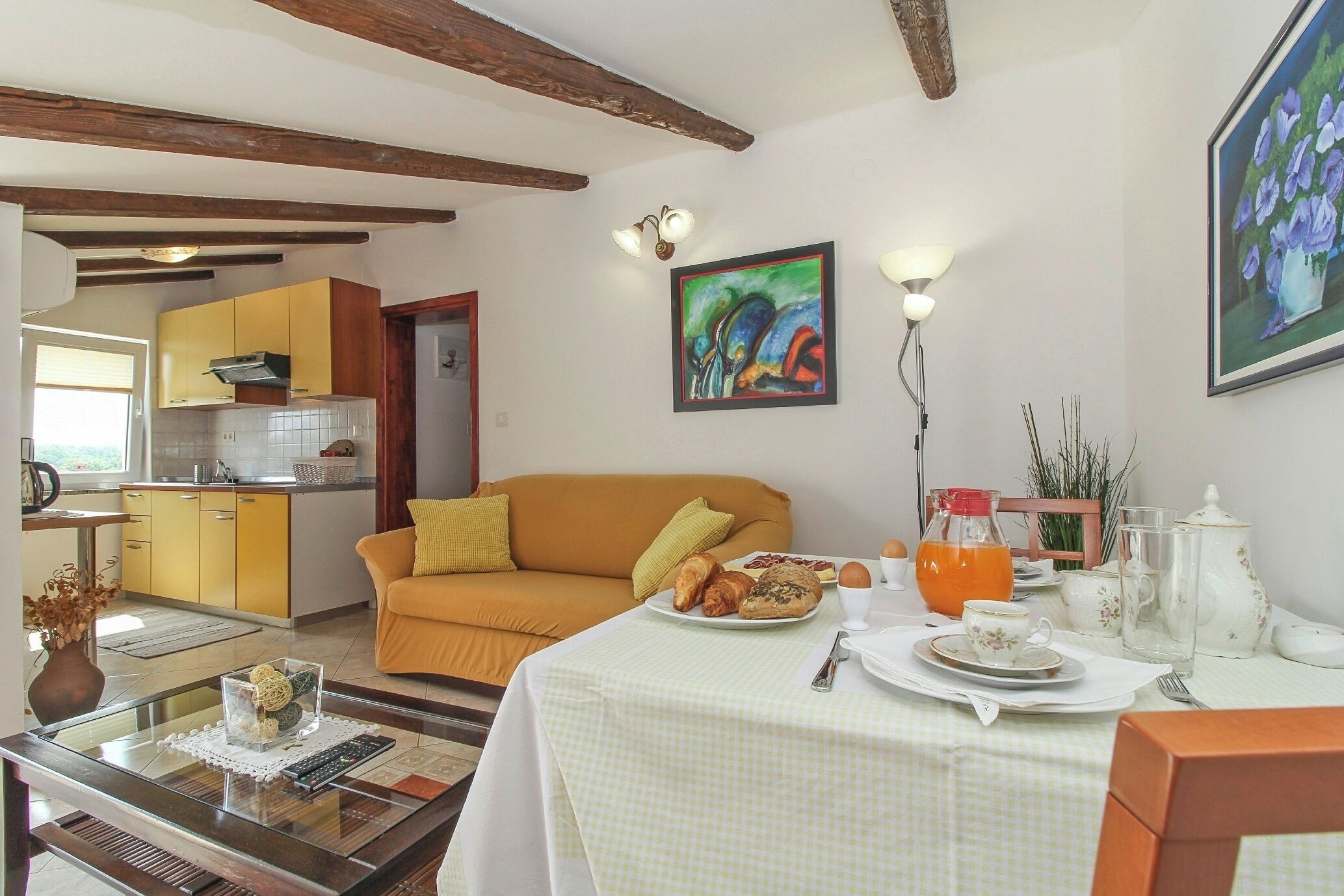 A dining area with a table set for breakfast, a sofa, and a kitchen in the background.
