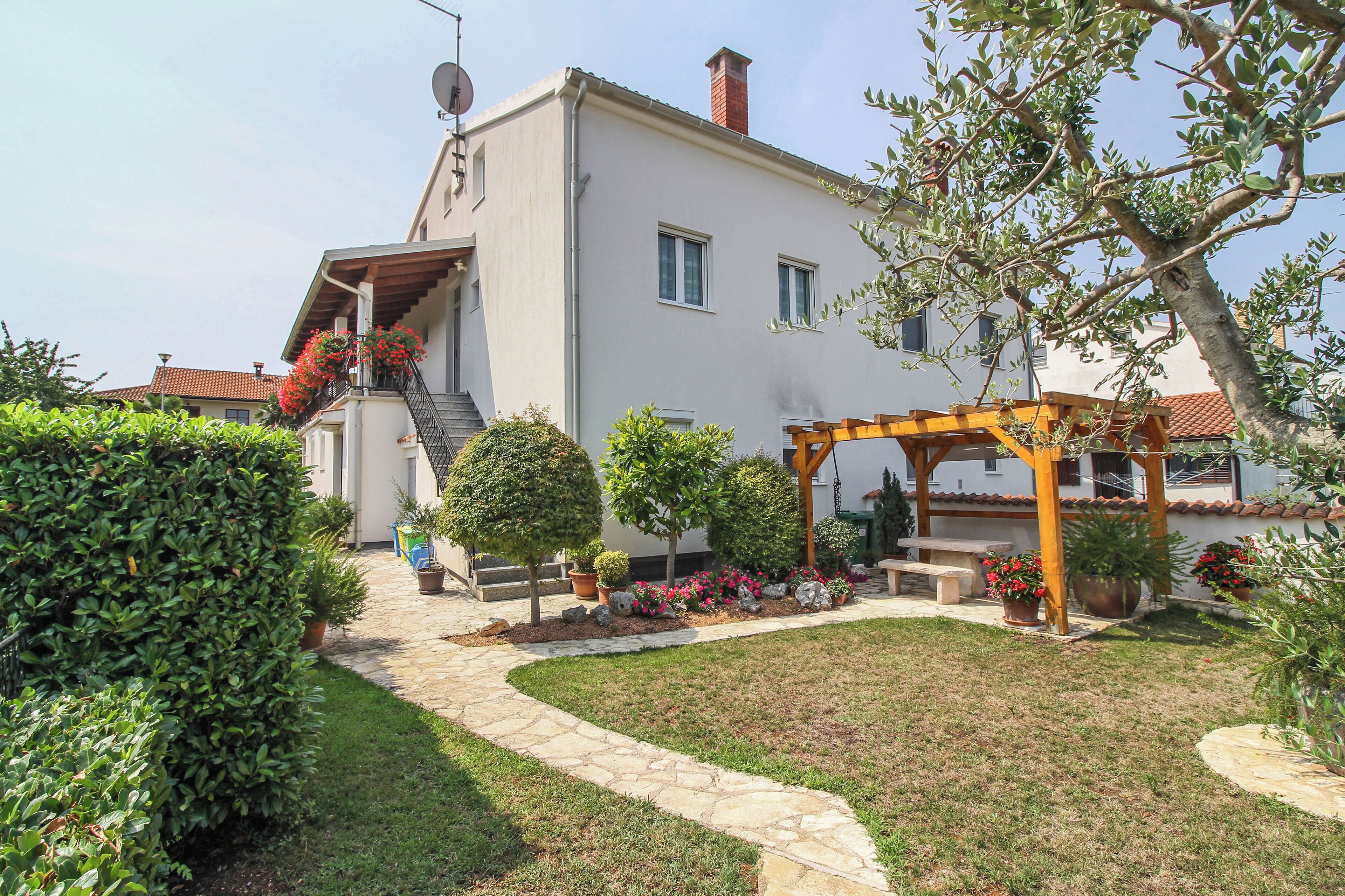 A two-story house with a stone pathway leading to a wooden pergola.
