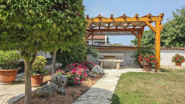 Un jardin agrémenté d’une pergola, de plantes en pot, d’un chemin de pierre et d’un banc en pierre.