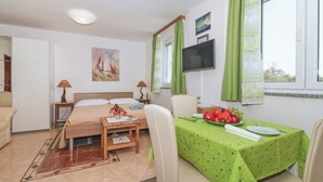Une chambre d’hôtel avec un lit, un bureau et une chaise, une table à manger recouverte d’une nappe verte et un téléviseur fixé au mur.