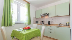 Une cuisine avec des meubles de couleur verte, un four à micro-ondes et un évier. On y trouve une table recouverte d’une nappe verte, ainsi que des chaises.