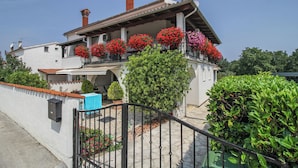 Une maison à deux étages dotée d’un balcon orné de fleurs rouges, d’une façade blanche et d’un toit recouvert de tuiles.
