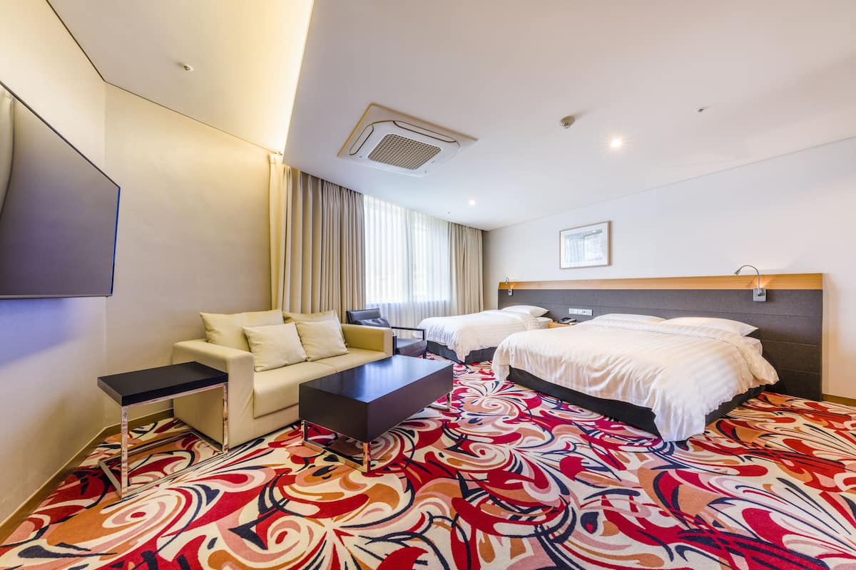 Ein Hotelzimmer mit zwei Betten, einem Sofa, einem Couchtisch und einem Fernseher.