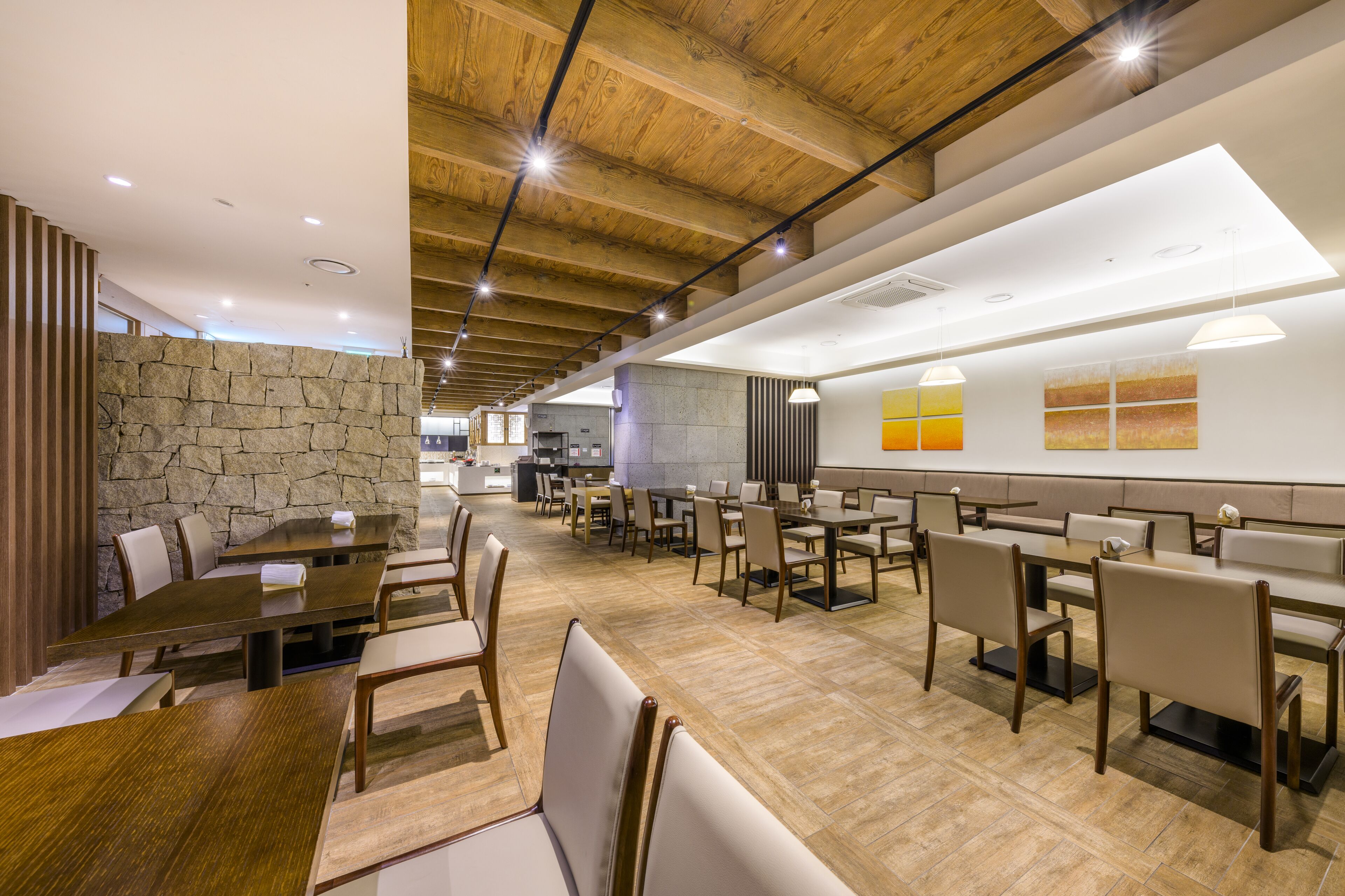 A spacious dining area with multiple tables and chairs, a stone wall, and a modern ceiling design.