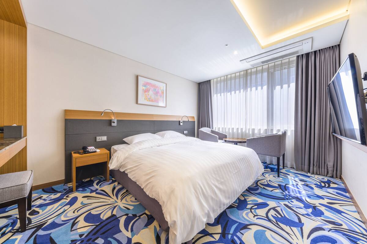 Ein Hotelzimmer mit einem großen Bett, einem Schreibtisch, einem Stuhl, einem kleinen Tisch und einem Fernseher.