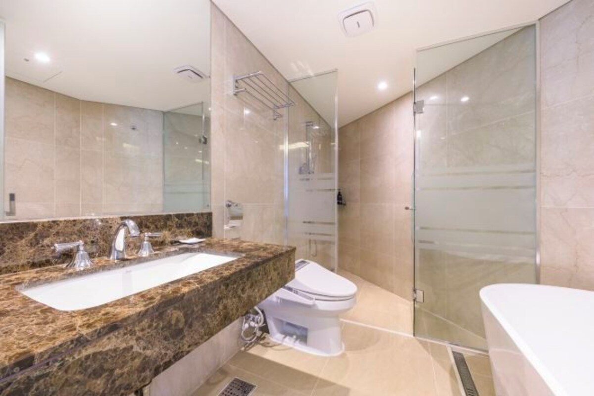 Une salle de bain moderne avec un lavabo surmonté d’un plan en granit, des toilettes blanches et une douche à parois de verre.