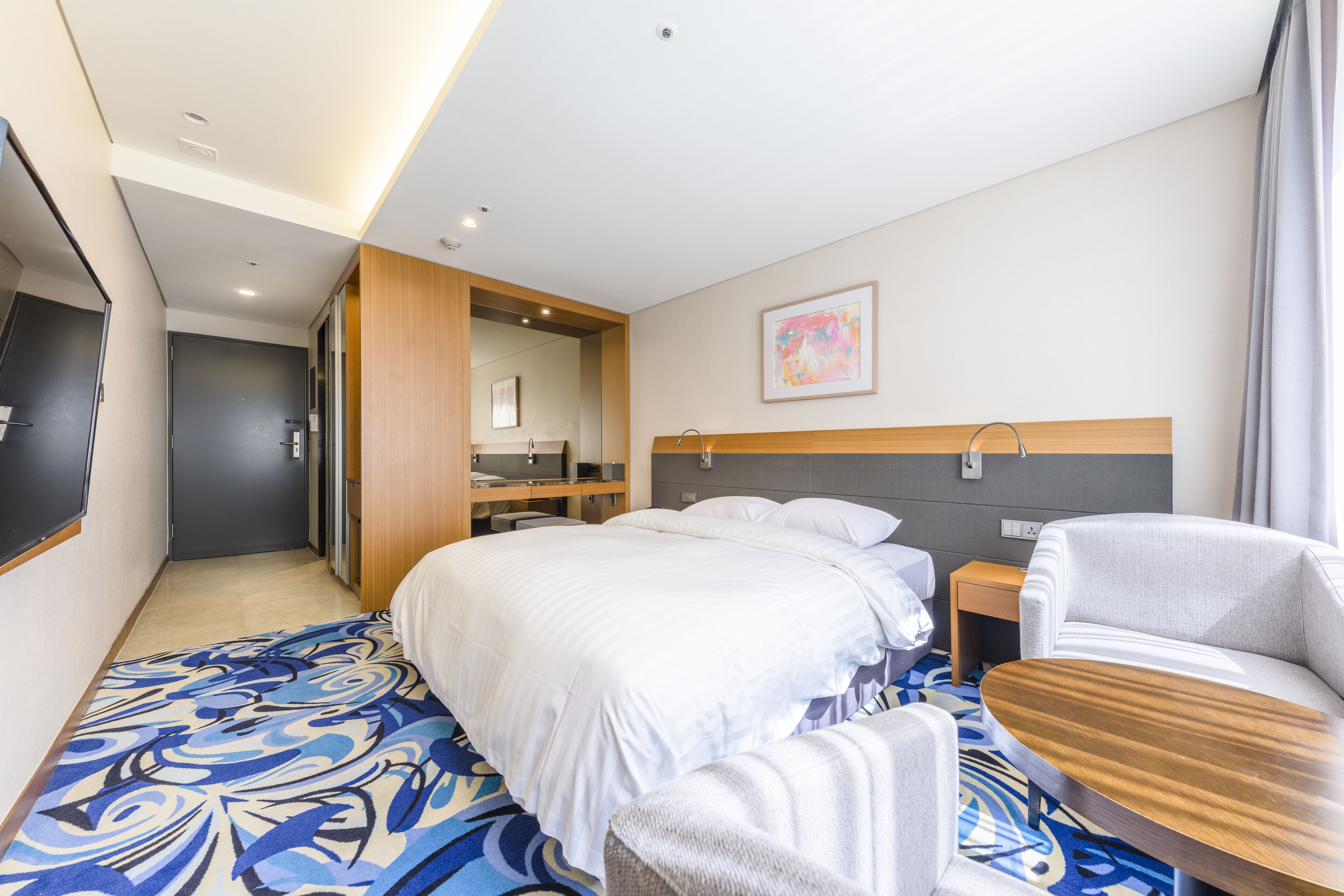 Habitación de hotel con una cama grande, una mesita de noche, una silla, un escritorio y un televisor.