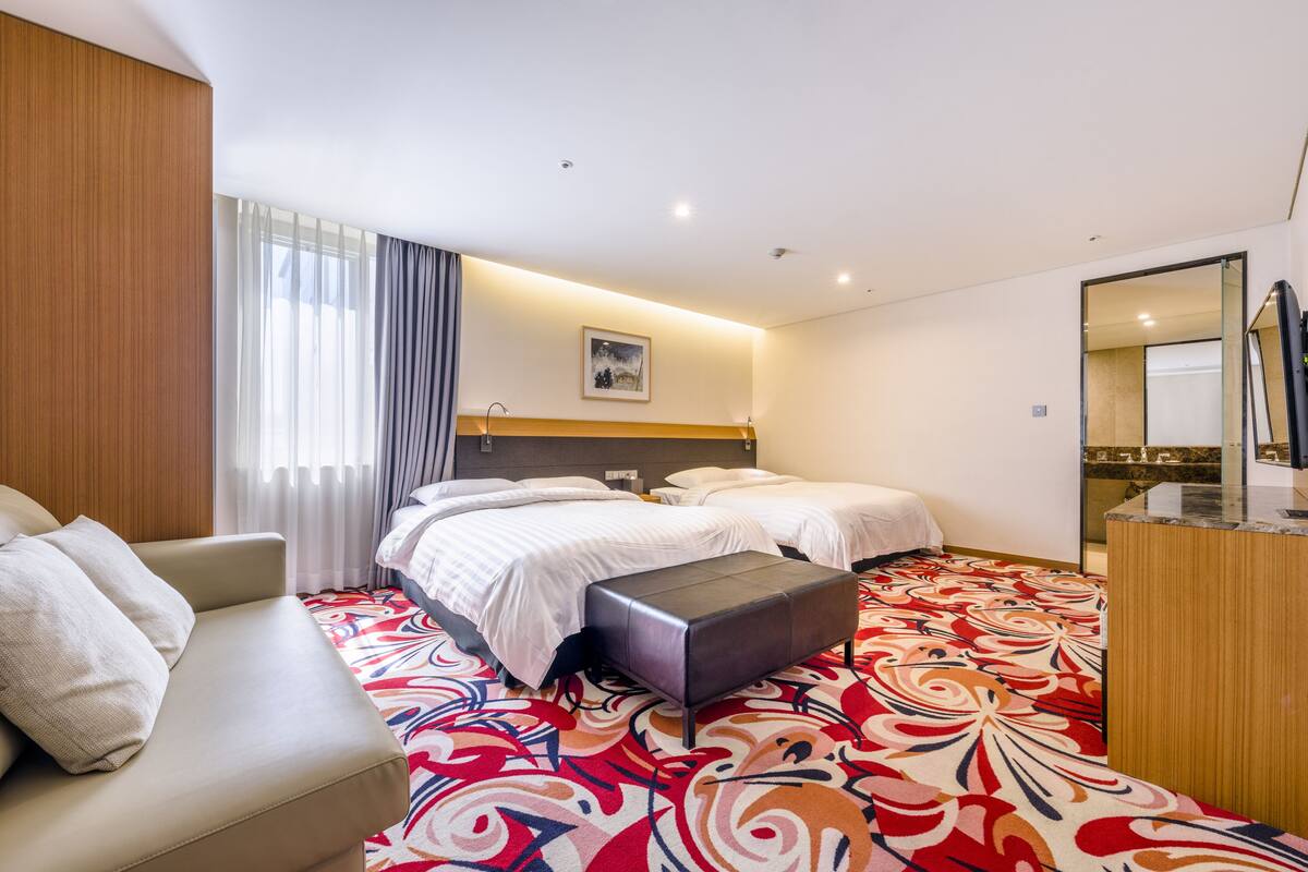 Ein Hotelzimmer mit zwei Betten, einem Schlafsofa, einem kleinen Tisch und Teppichboden.