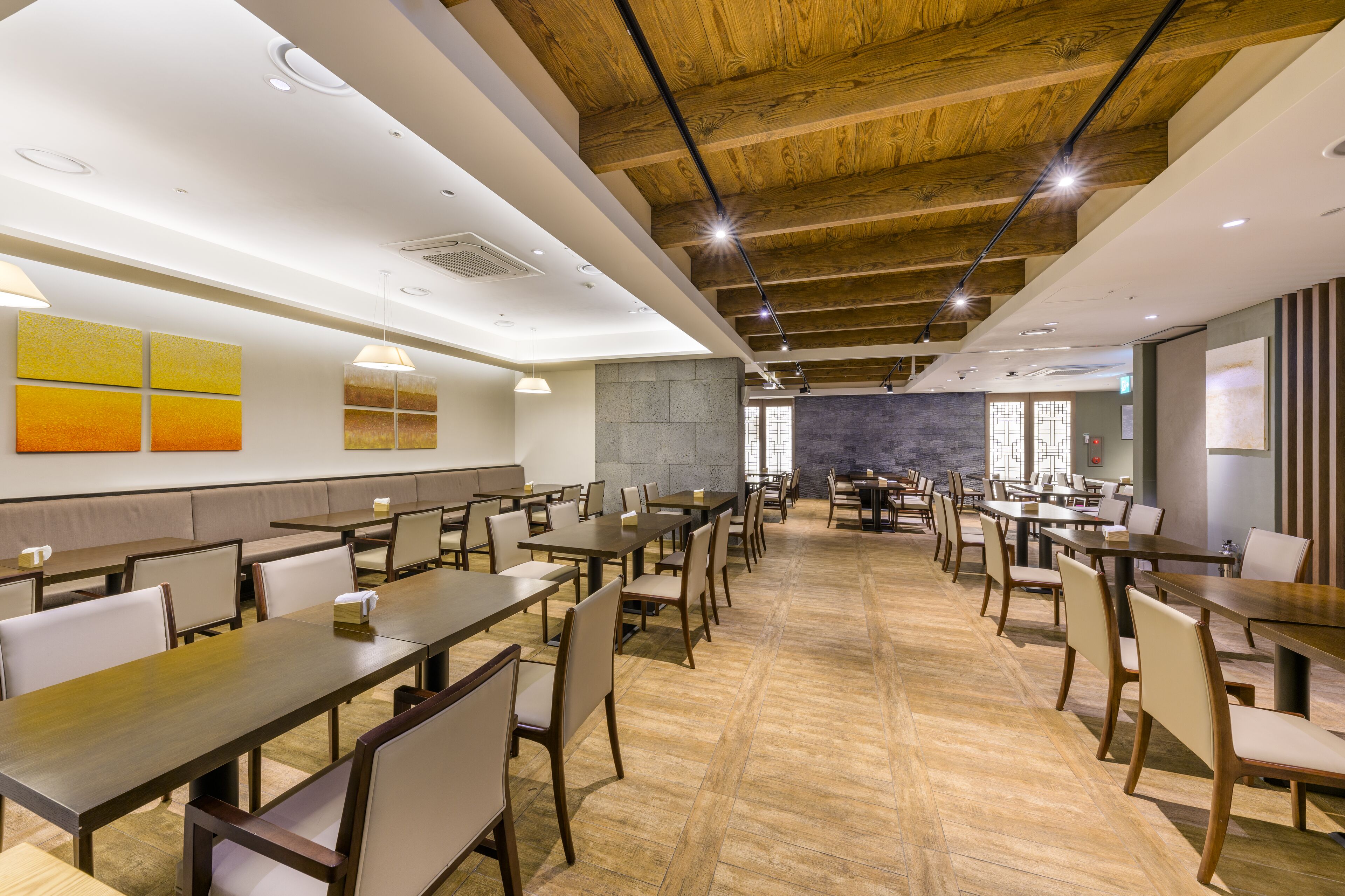 A spacious dining area with multiple tables and chairs, wooden ceiling beams, and a modern interior design.
