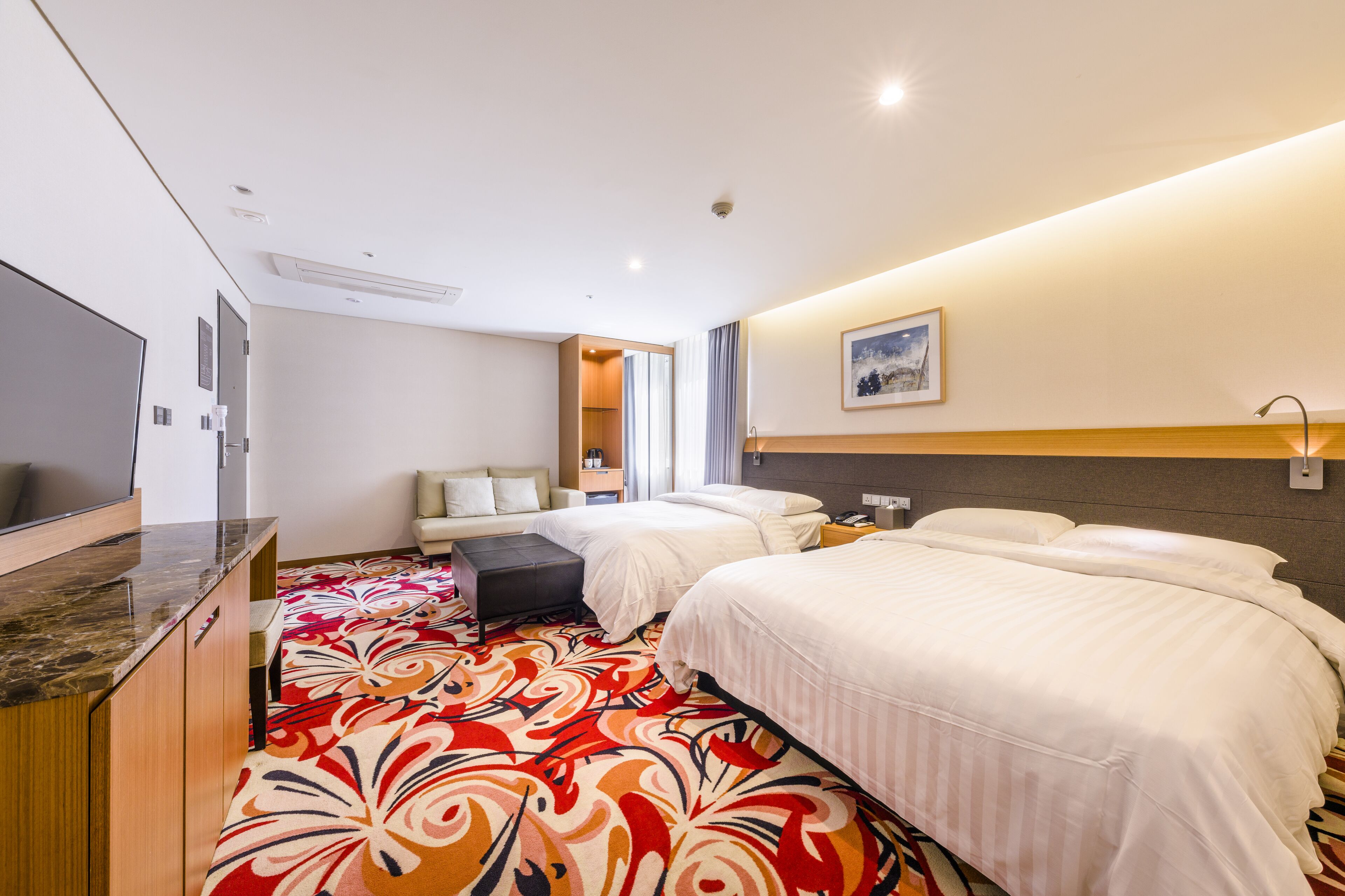 Une chambre d’hôtel avec deux lits, une télévision, un bureau et une moquette colorée.