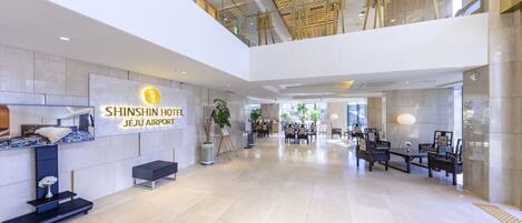 A spacious lobby with a reception desk, seating area, and a sign for Shinshin Hotel Jeju Airport.