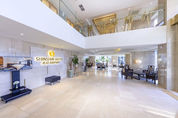 Un amplio vestíbulo con mostrador de recepción, zona de estar y cartel del Hotel Shinshin Jeju Airport.