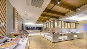 Un espace buffet proposant différents types de plats, avec un aménagement moderne agrémenté de poutres en bois au plafond.