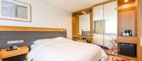 A hotel room with a large bed, a bedside table with a phone, a mirror, a TV, and a coffee machine.