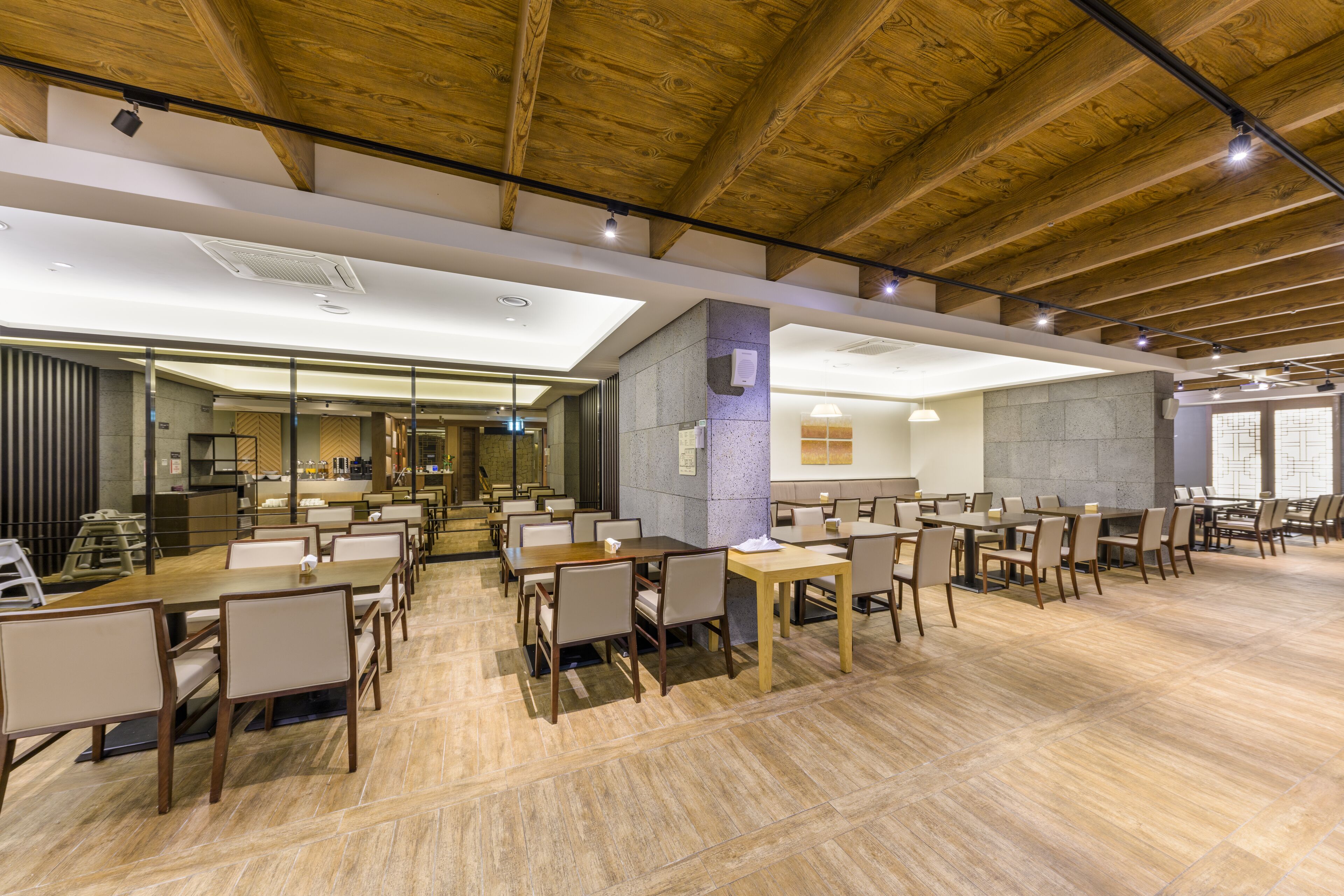 A spacious dining area with multiple tables and chairs, a high ceiling with exposed beams, and a modern interior design.
