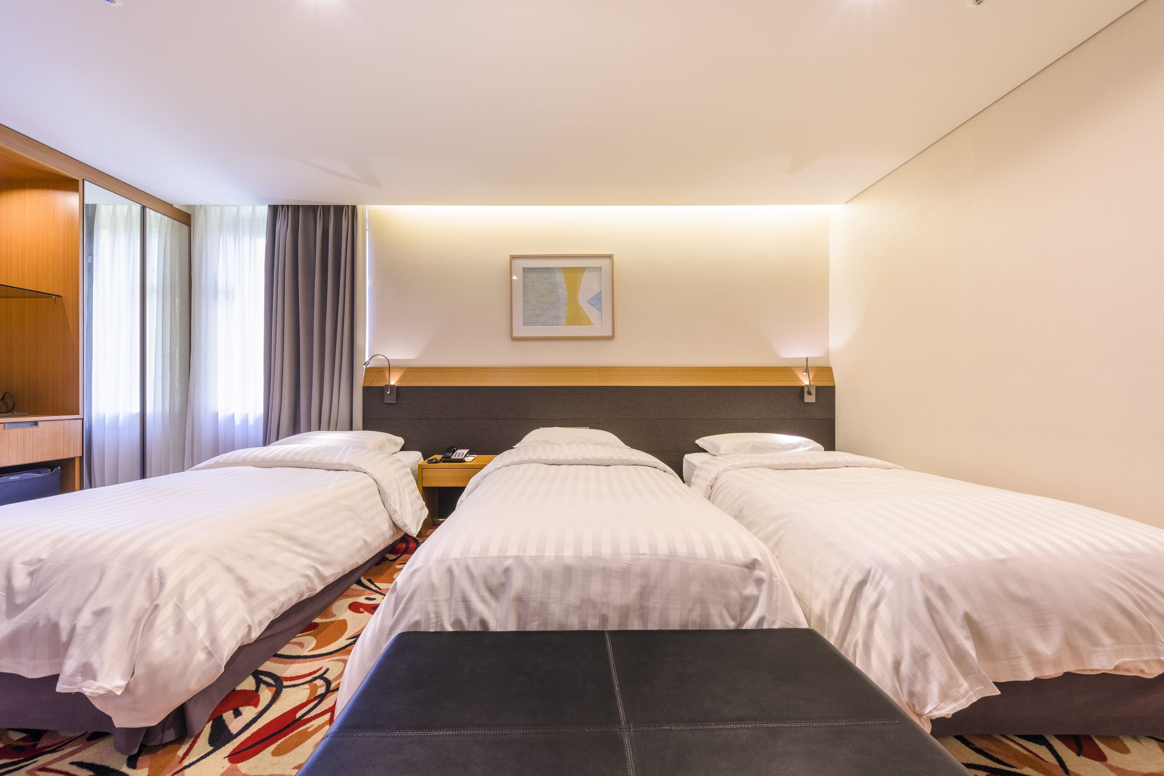 A hotel room with two single beds, a desk, and a bench.