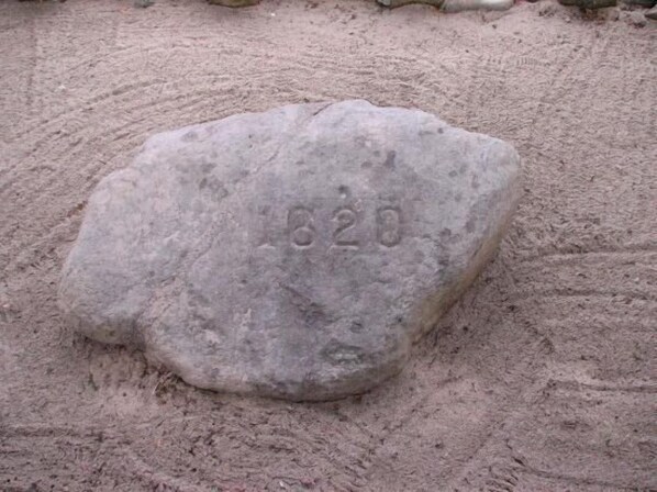 A large, rough-textured stone with the number "1820" engraved on it, placed on a sandy surface.