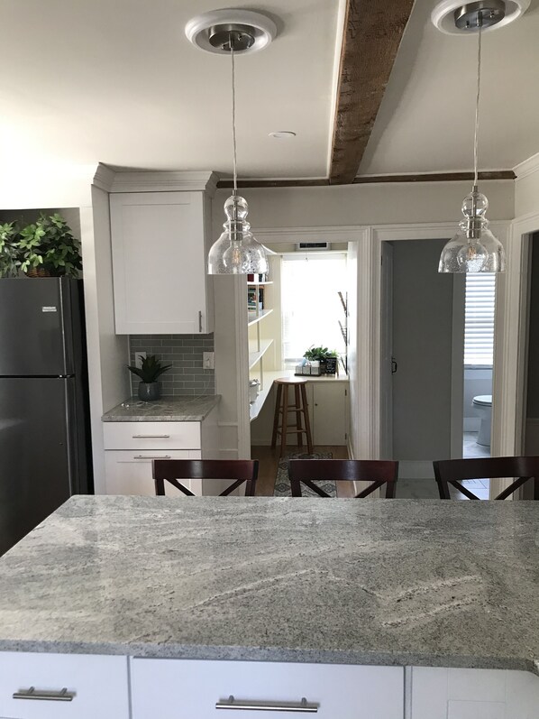 A kitchen with granite countertops, white cabinets, and hanging pendant lights.