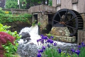 Un puente de piedra rústico con una noria grande, una cascada pequeña e iris púrpuras en primer plano.