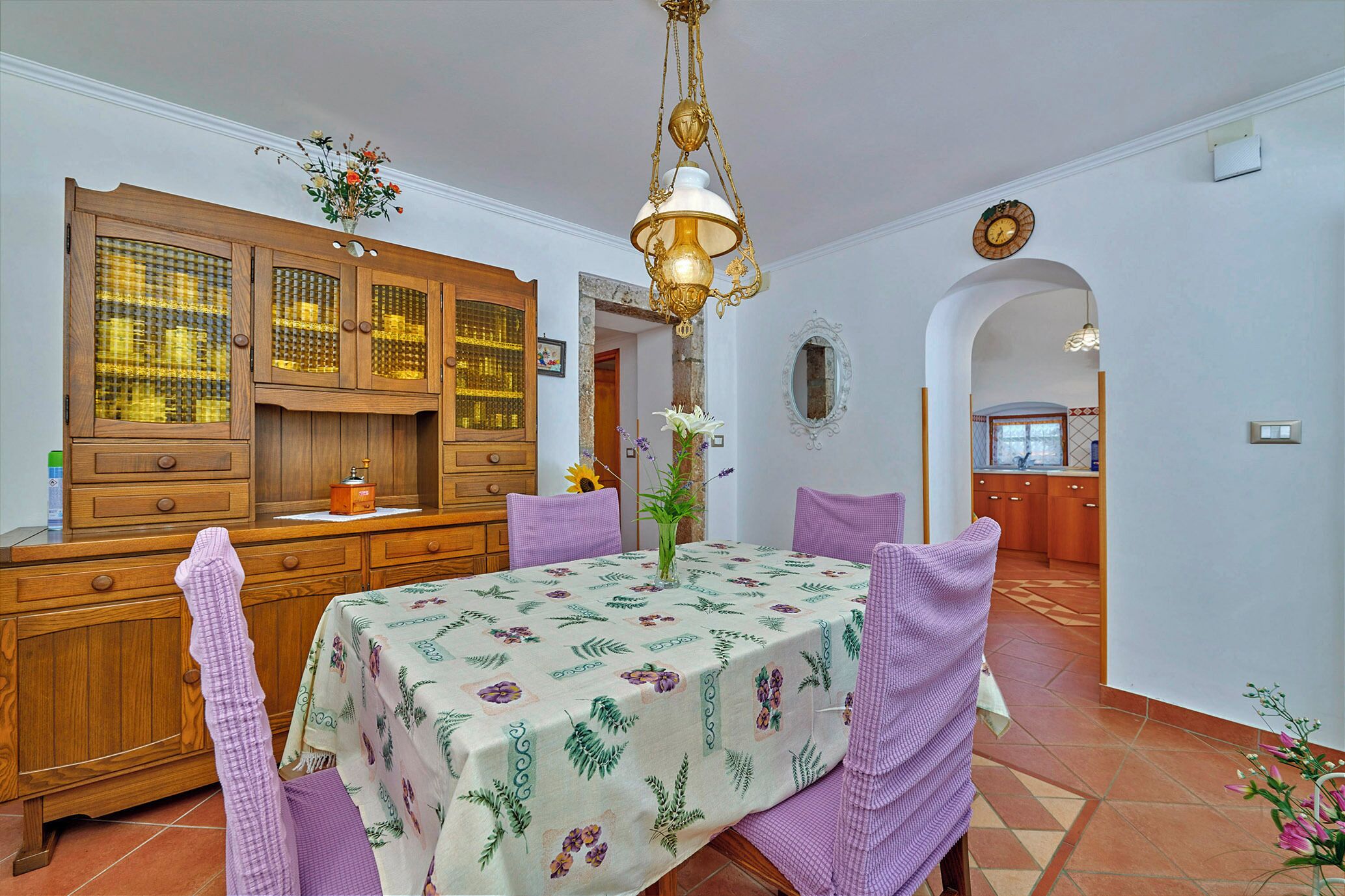 A dining area with a table set for four, surrounded by purple chairs, a wooden cabinet with glass doors, and a hanging chandelier.