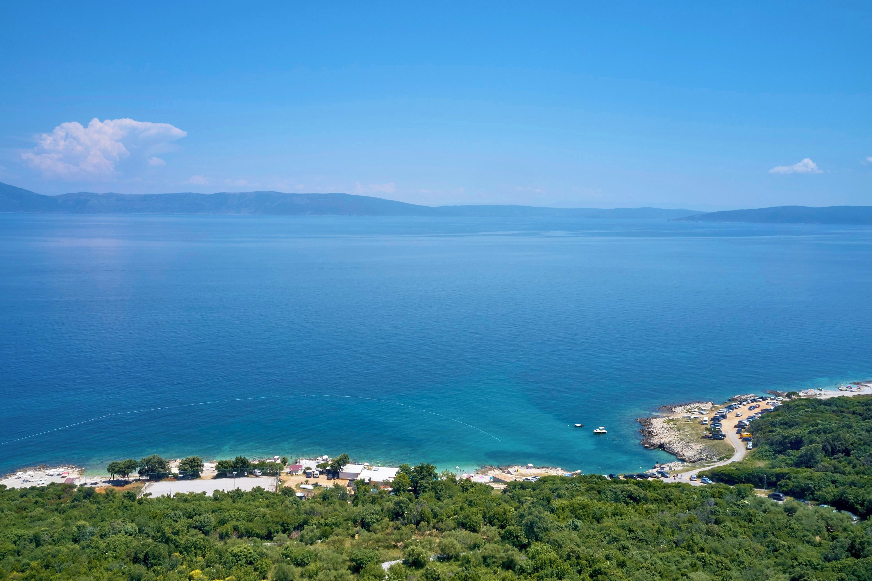 A coastal area with a clear view of the sea, a small beach, and a parking area.