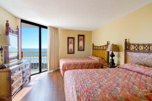 Ein Hotelzimmer mit zwei Betten, einem Schminktisch, einem Nachttisch und Blick aufs Meer.