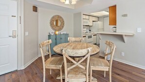 A dining area with a round wooden table and four chairs, a decorative mirror, and a kitchen in the background.
