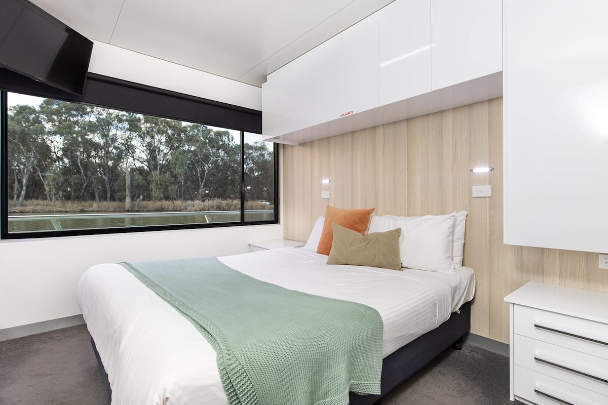 Une chambre moderne avec un grand lit, une vue sur les arbres par la fenêtre et des meubles encastrés.