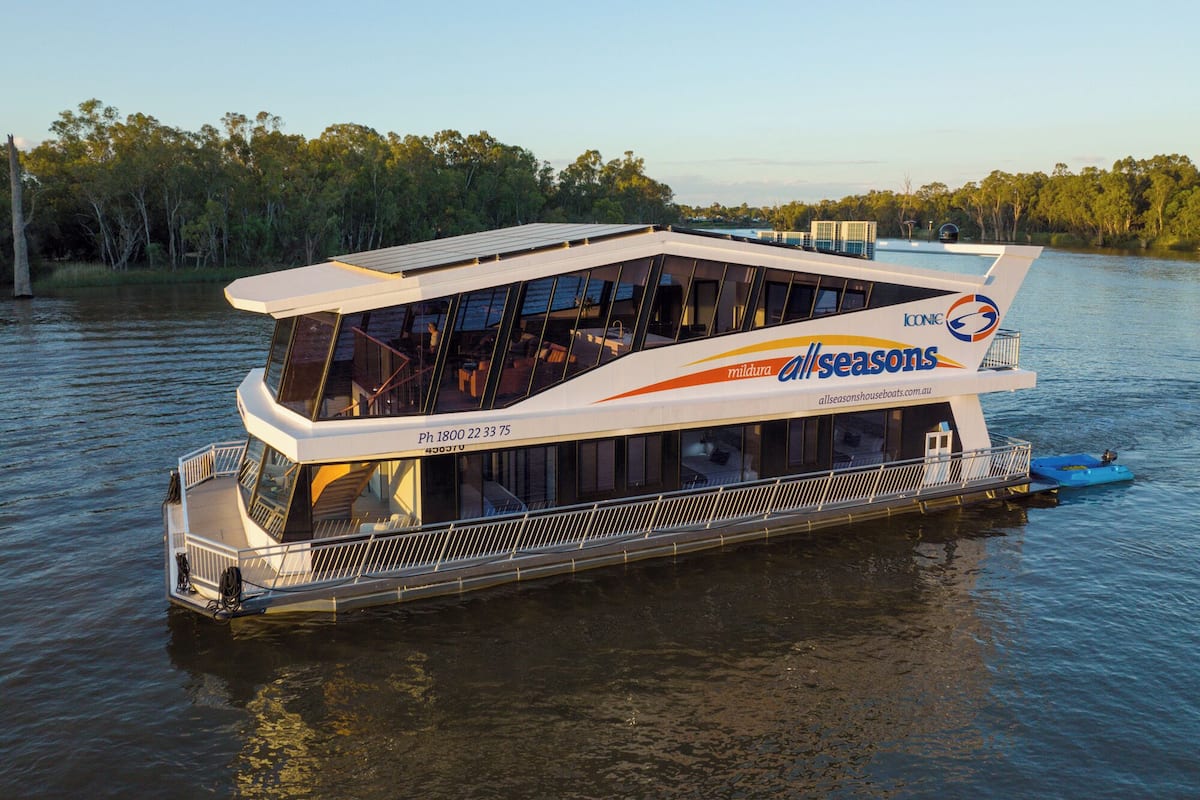 Une péniche dotée d’une grande terrasse, de nombreuses fenêtres et d’un logo indiquant qu’elle est utilisable « en toutes saisons ».