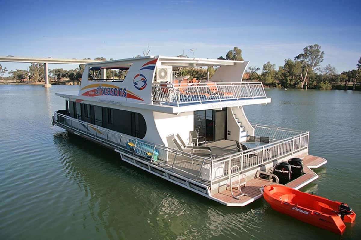 Un grand bateau à plusieurs ponts, doté d’un pont supérieur couvert et d’un pont inférieur à ciel ouvert, était amarré sur une rivière paisible.
