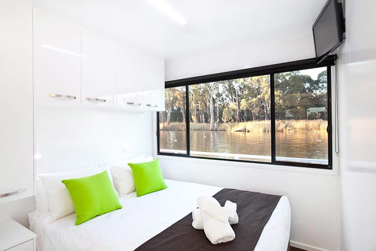 Une chambre d’hôtel moderne avec un grand lit, des oreillers verts, une vue sur un lac et un téléviseur à écran plat fixé au mur.