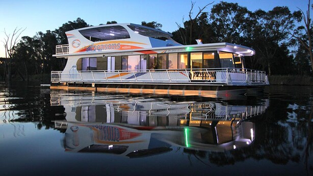 Un'ampia houseboat moderna con un ampio ponte e numerose finestre, che galleggia su acque calme.