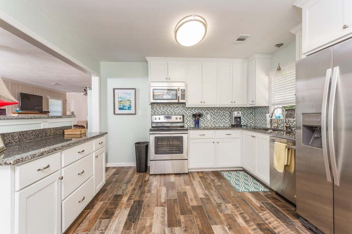 A kitchen with white cabinets, a stainless steel refrigerator, a microwave, an oven, and a tiled backsplash.